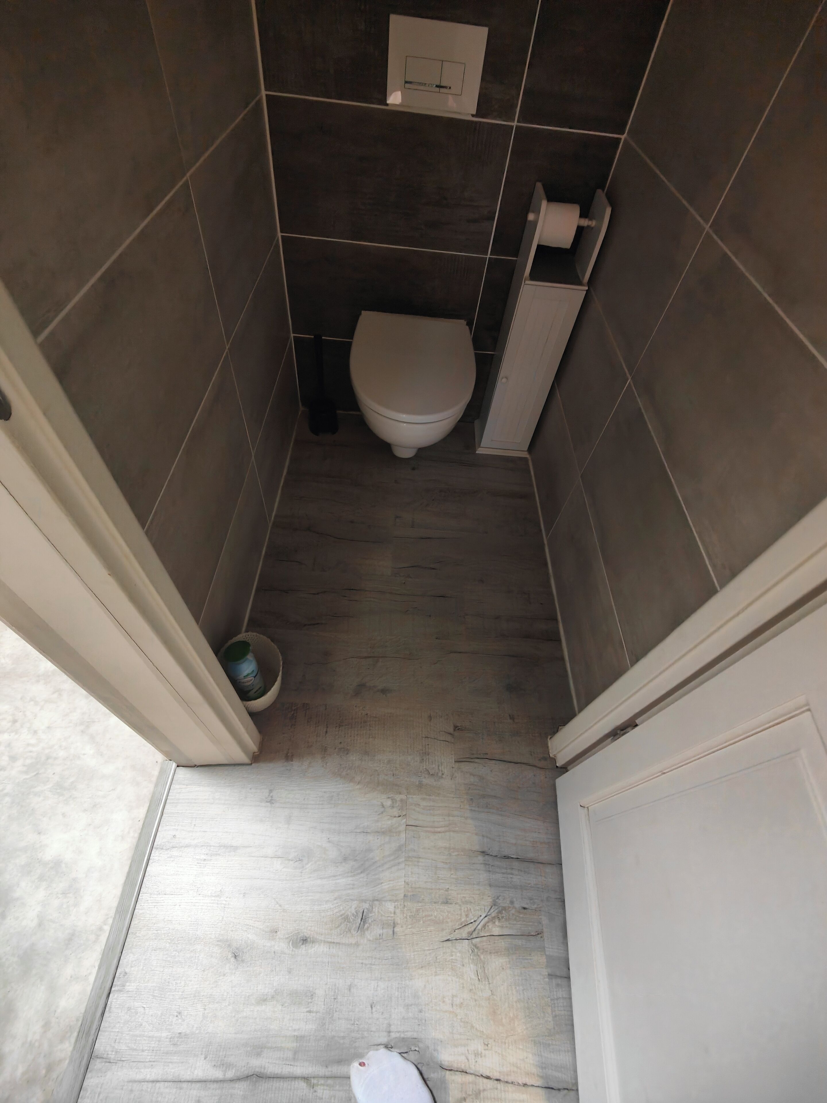 A small, narrow bathroom with a toilet, a toilet paper holder, and a small trash bin.
