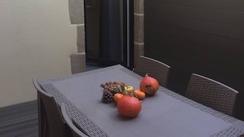 An outdoor patio with a table set for two, featuring wicker chairs and a tablecloth.