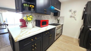 A kitchen with black cabinets, a red microwave, a gas stove, and a refrigerator. - Ideally located, easy access, & stunning city views! with king size bed. (Alhambra)