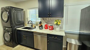 A kitchen with a washing machine, a sink, a dishwasher, and a trash can. - Ideally located, easy access, & stunning city views! with king size bed. (Alhambra)