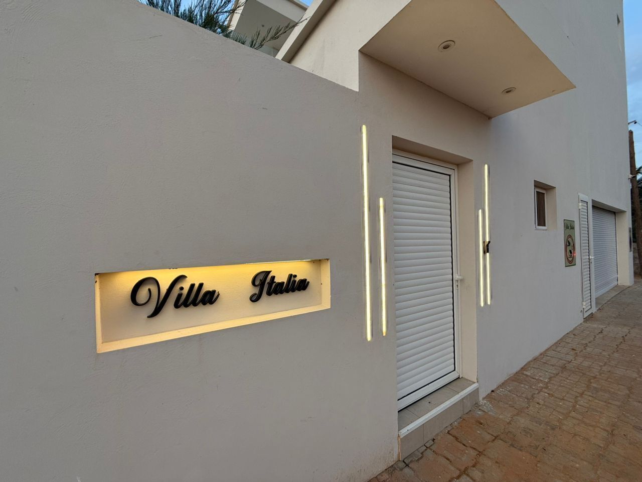 Een moderne villa met een bordje met de tekst 'Villa Italia' en een gesloten luik.