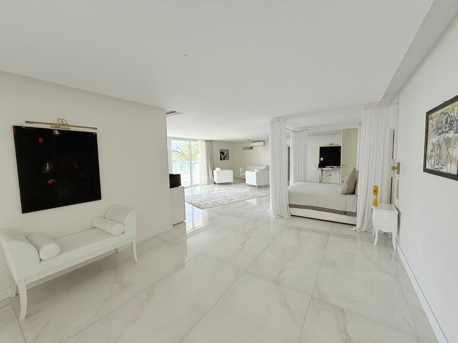 A spacious, modern bedroom with a large bed, a white sofa, and a flat-screen TV.