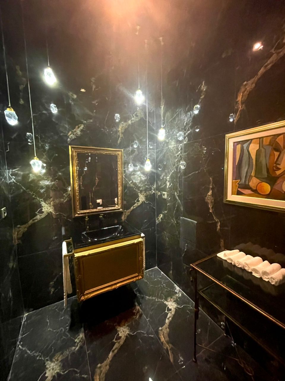 A bathroom with a black marble sink, a gold vanity, and a marble floor.