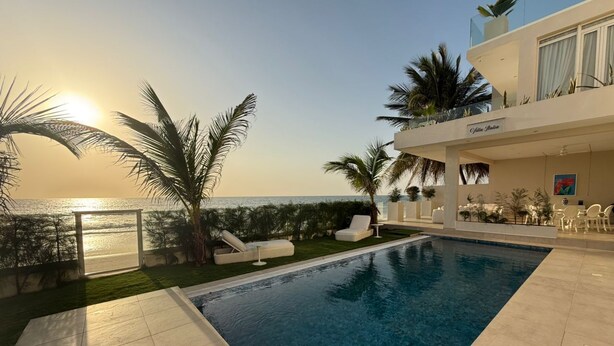 Piscina com vista para o mar, cadeiras de praia e palmeiras.