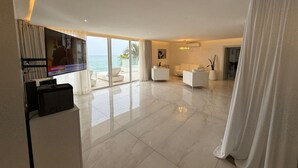 Uma sala de estar moderna com televisão de tela plana, mobiliário branco e vista para o oceano.