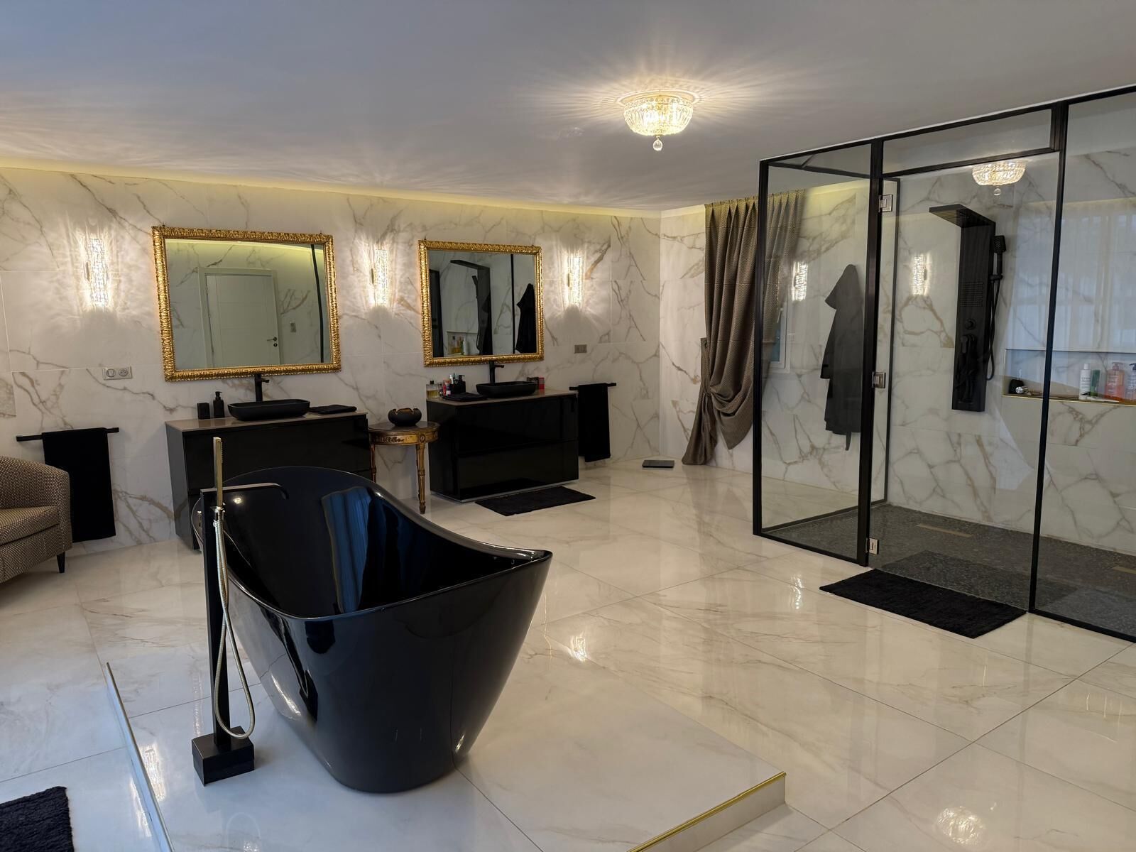A modern bathroom with a large mirror, two sinks, a black bathtub, and a glass shower enclosure.