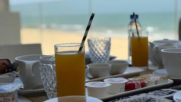 A breakfast setting with a table set for two, featuring a glass of orange juice, a white mug, and a tray with food items.
