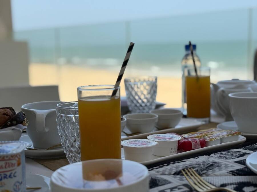 A breakfast setting with a table set for two, featuring a glass of orange juice, a white mug, and a tray with food items.