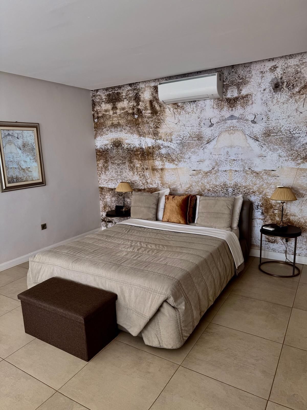 A bedroom with a large bed, a nightstand, a lamp, and a textured wall.