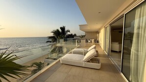 Ein Balkon mit Meerblick, ausgestattet mit weißen Liegestühlen und einem Glasgeländer.
