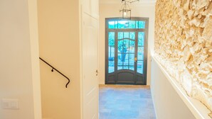 Un pasillo con pared de piedra, una puerta con paneles de vidrio y una escalera con escalones color beige.