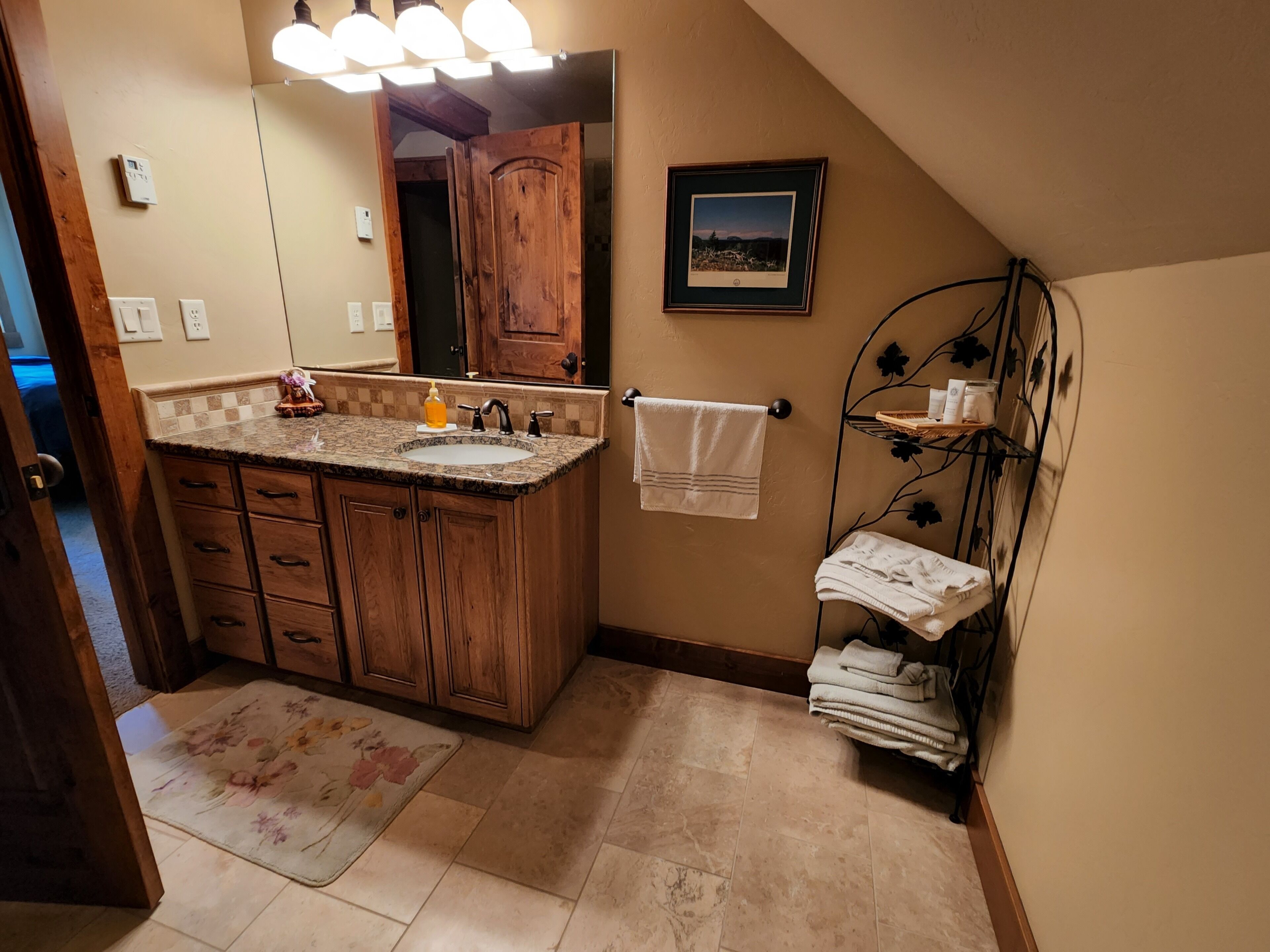 A bathroom with wooden cabinets, a granite countertop, a sink, a mirror, a towel rack, and a framed picture on the wall.