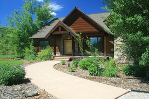 A modern log cabin with a stone foundation, a wooden front porch, and a landscaped garden with a concrete pathway leading to the entrance.