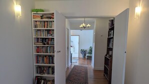 A hallway with open bookshelves, a patterned rug, and a chandelier.