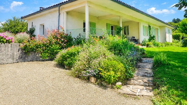 A two-story house with a covered porch, a gravel driveway, and a garden with various plants and flowers.
