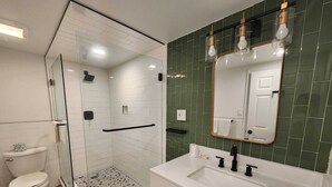 A modern bathroom with a glass-enclosed shower, a white sink with a black faucet, and a mirror with a gold frame. - Westview Motel (North Bergen)