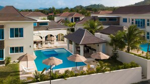 Ein Resort mit Swimmingpool, umgeben von Liegestühlen und Sonnenschirmen, moderner Architektur und Blick auf die Berge.