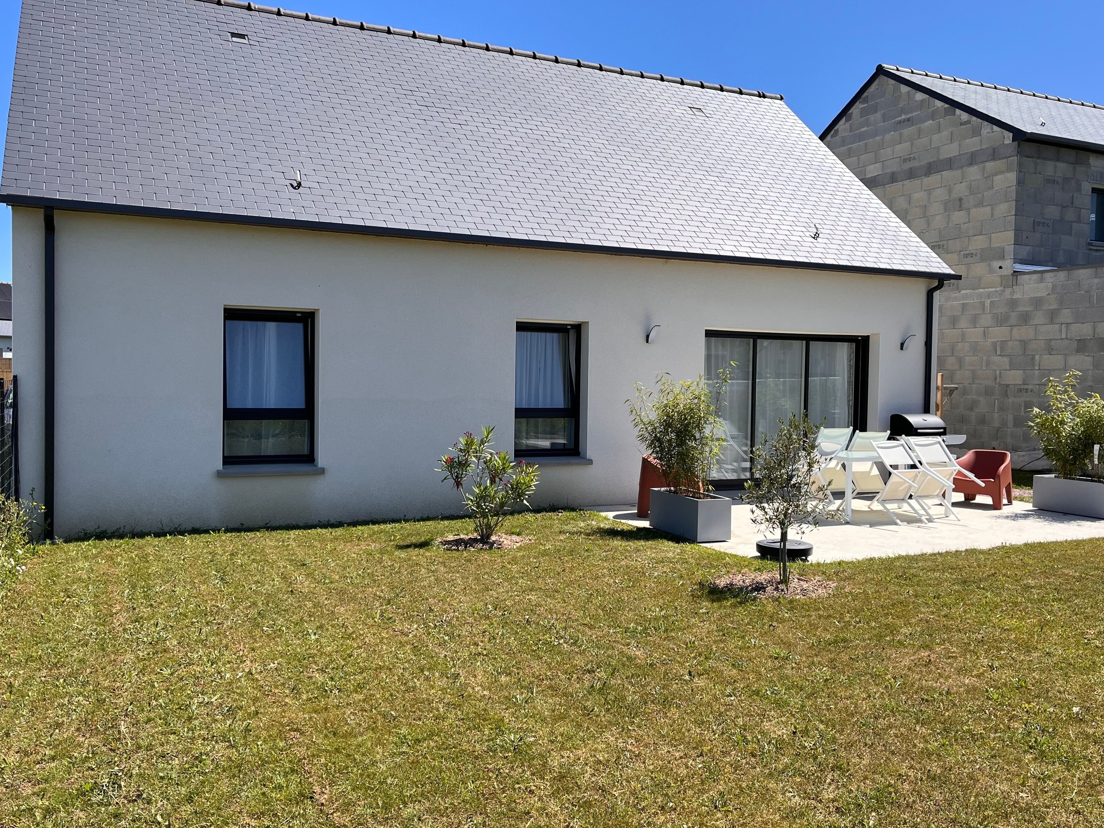 Une maison moderne à deux étages, dotée d’un toit plat, d’un patio avec mobilier d’extérieur et d’un petit jardin.
