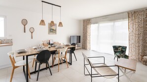 Ein moderner Essbereich mit Holztisch, schwarzen und weißen Stühlen, hängenden Korbtischen und einem Fernseher auf einem Beistelltisch.