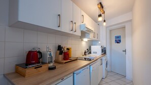 A compact kitchen with white cabinets, a wooden countertop, a red kettle, a microwave, and a washing machine.