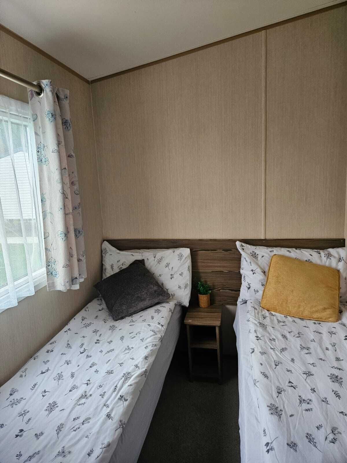 A small, compact room with two single beds, a small table, and a window with curtains.