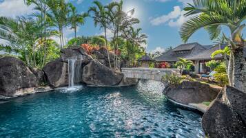 A tropical resort with a clear pool, a waterfall, and lush greenery.