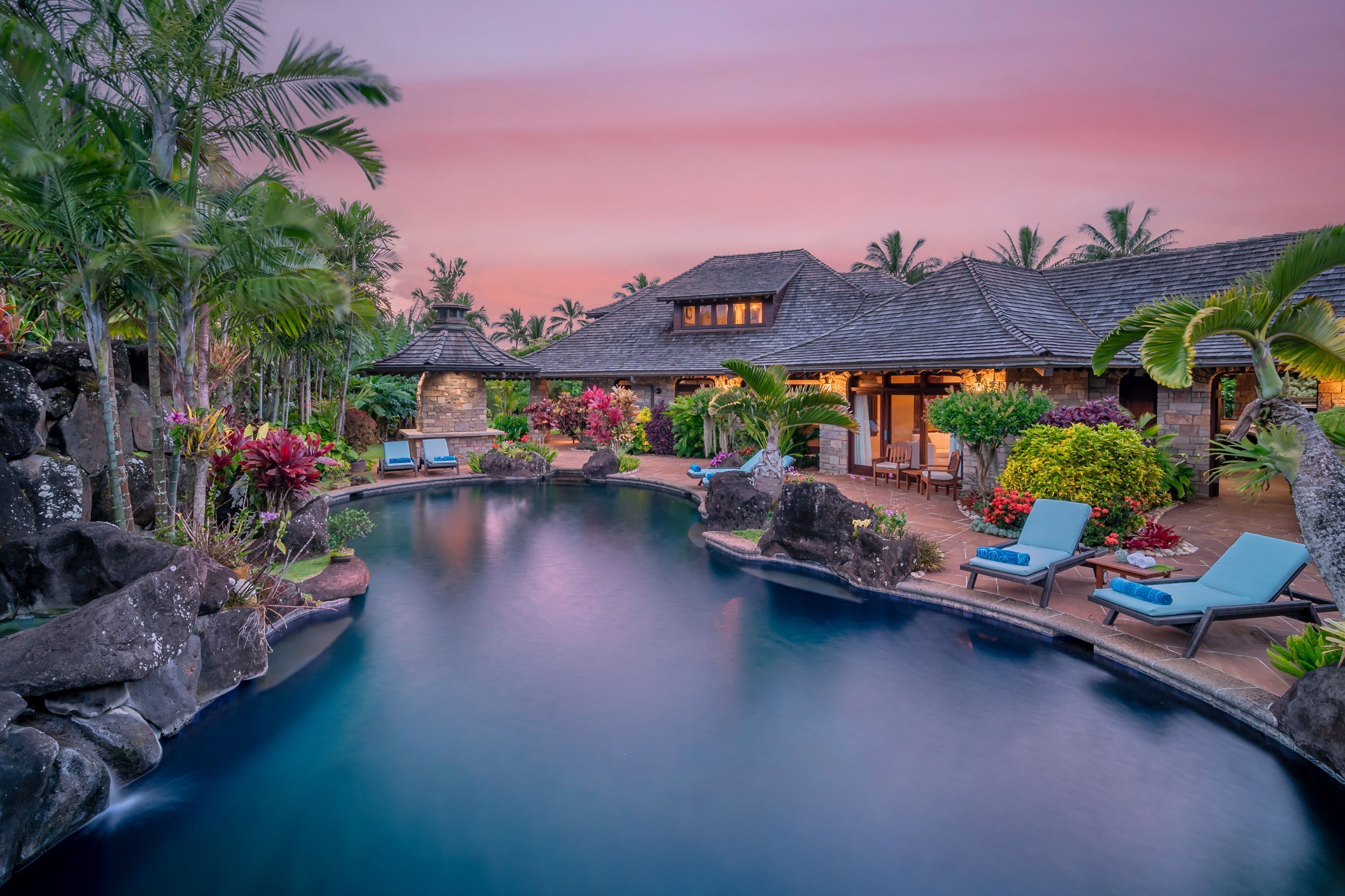 A pool area with lounge chairs and a stone building with a tiled roof.