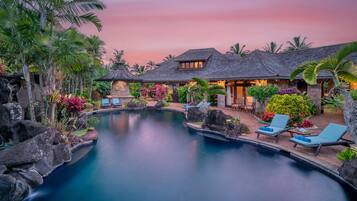 A pool area with lounge chairs and a stone building with a tiled roof.