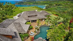 Une grande maison avec une piscine, entourée d’une végétation luxuriante et offrant une vue sur l’océan.