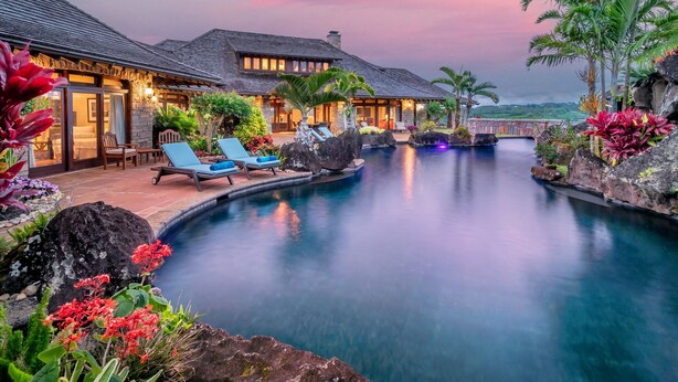 Un complexe hôtelier doté d’une piscine, de chaises longues et d’un aménagement paysager de style tropical.