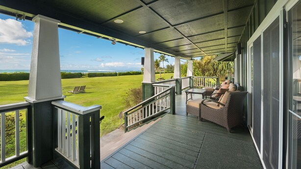 Ein überdachter Balkon mit Blick auf eine grüne Wiese und einen klaren Himmel.