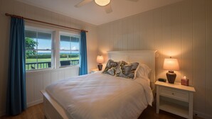 Ein Schlafzimmer mit einem Bett, zwei Nachttischlampen, einem Nachttisch, einem Deckenventilator und einem Fenster mit Vorhängen.