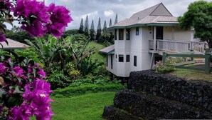A two-story building with a balcony, surrounded by lush greenery and a stone wall. - Hanalei Bay Villa 8 (Princeville)