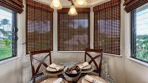 A dining area with a round table set for four, featuring a bowl of fruit and folded napkins. - Hanalei Bay Villa 8 (Princeville)