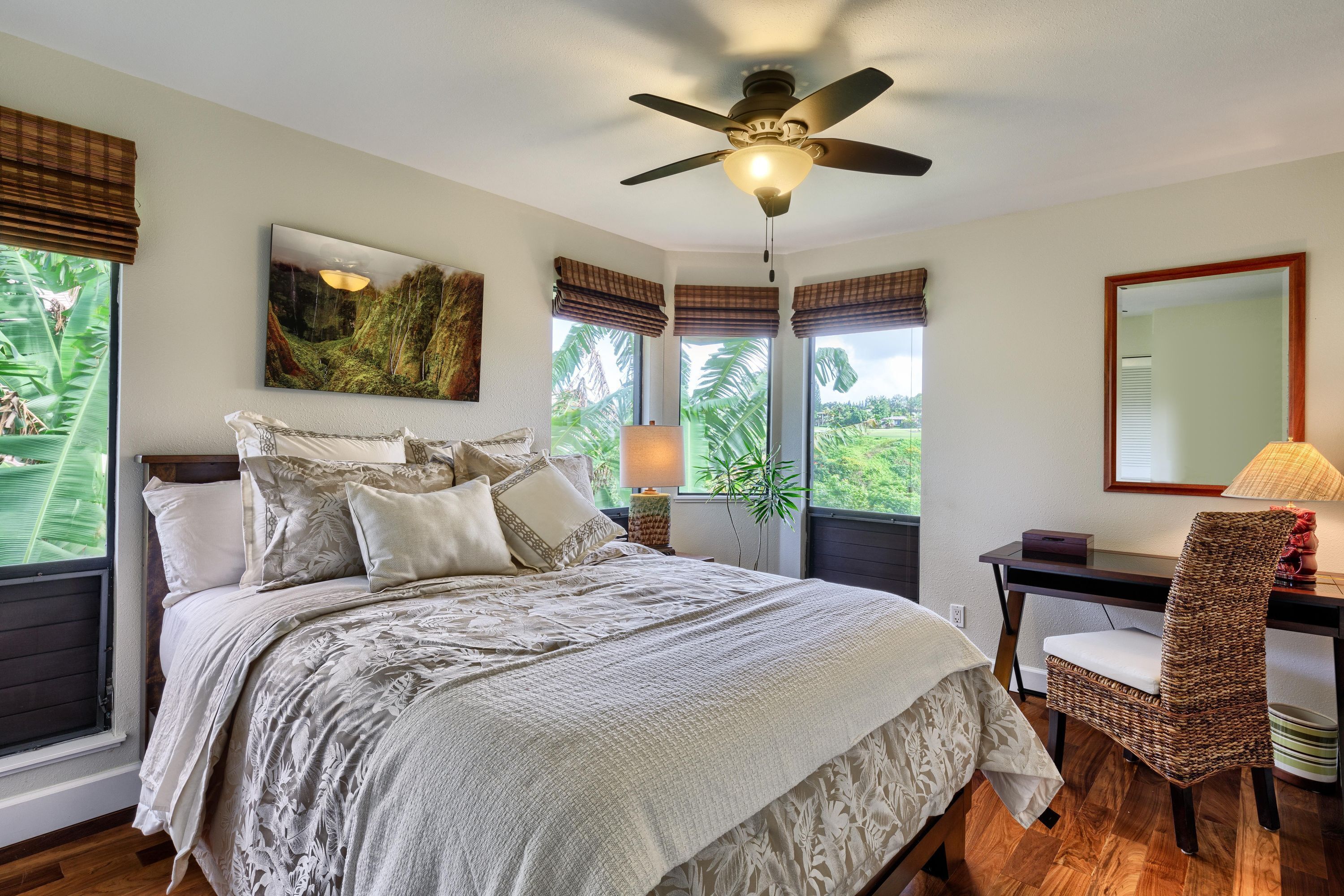 A bedroom with a large bed, a desk, a chair, a ceiling fan, and windows with curtains.