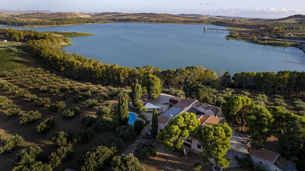 Vista aérea de una propiedad con piscina, paneles solares y una extensa masa de agua.