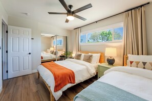 A hotel room with a bed, bedside table, lamp, window with curtains, and a ceiling fan.