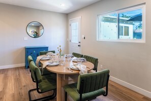 Un coin repas avec une table ronde, des chaises à revêtement vert et un buffet bleu.