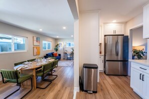 A modern kitchen with a stainless steel refrigerator, wooden dining table with chairs, and a view to the backyard.