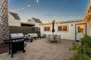 Un jardin avec un barbecue, des meubles pour s’asseoir à l’extérieur et des guirlandes lumineuses.