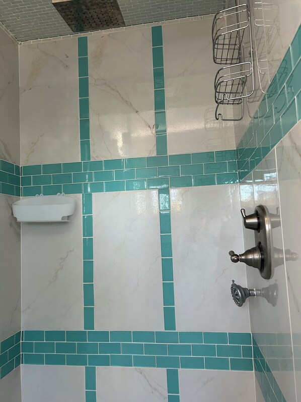 A bathroom with white marble tiles and teal accents, a white towel rack, and a shower control knob.