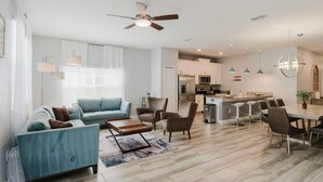 A modern living room with a sofa, chairs, a coffee table, and a dining area with a table and chairs. There is a kitchen in the background with appliances and a ceiling fan. - Last Minute Disney Getaway! Private Pool & Themed Bedrooms. Book Now! #122403 (Orlando)