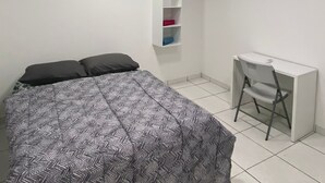 Une chambre à coucher comprenant un lit, un bureau, une chaise, un climatiseur et une étagère suspendue.