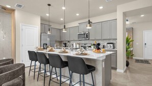 Une cuisine moderne avec des meubles gris, un îlot central doté de tabourets de bar, des appareils en acier inoxydable et un éclairage suspendu.