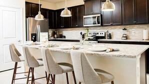 Una cocina moderna con armarios de madera oscura, una isla grande con taburetes de bar, electrodomésticos de acero inoxidable e iluminación colgante.