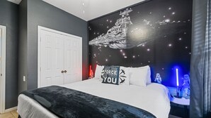A bedroom with a bed, a wall mural of a spaceship, and Star Wars-themed decor.