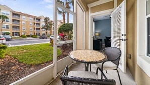 A balcony with a table and chairs, overlooking a parking lot and a building with balconies.