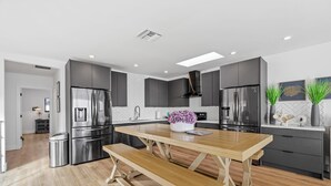 Una cocina moderna con armarios grises, electrodomésticos de acero inoxidable, una mesa de comedor de madera y un banco.