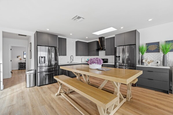A modern kitchen with grey cabinetry, stainless steel appliances, a wooden dining table, and a bench. - Carlsbad Beachfront Home W Hot tub (Carlsbad)