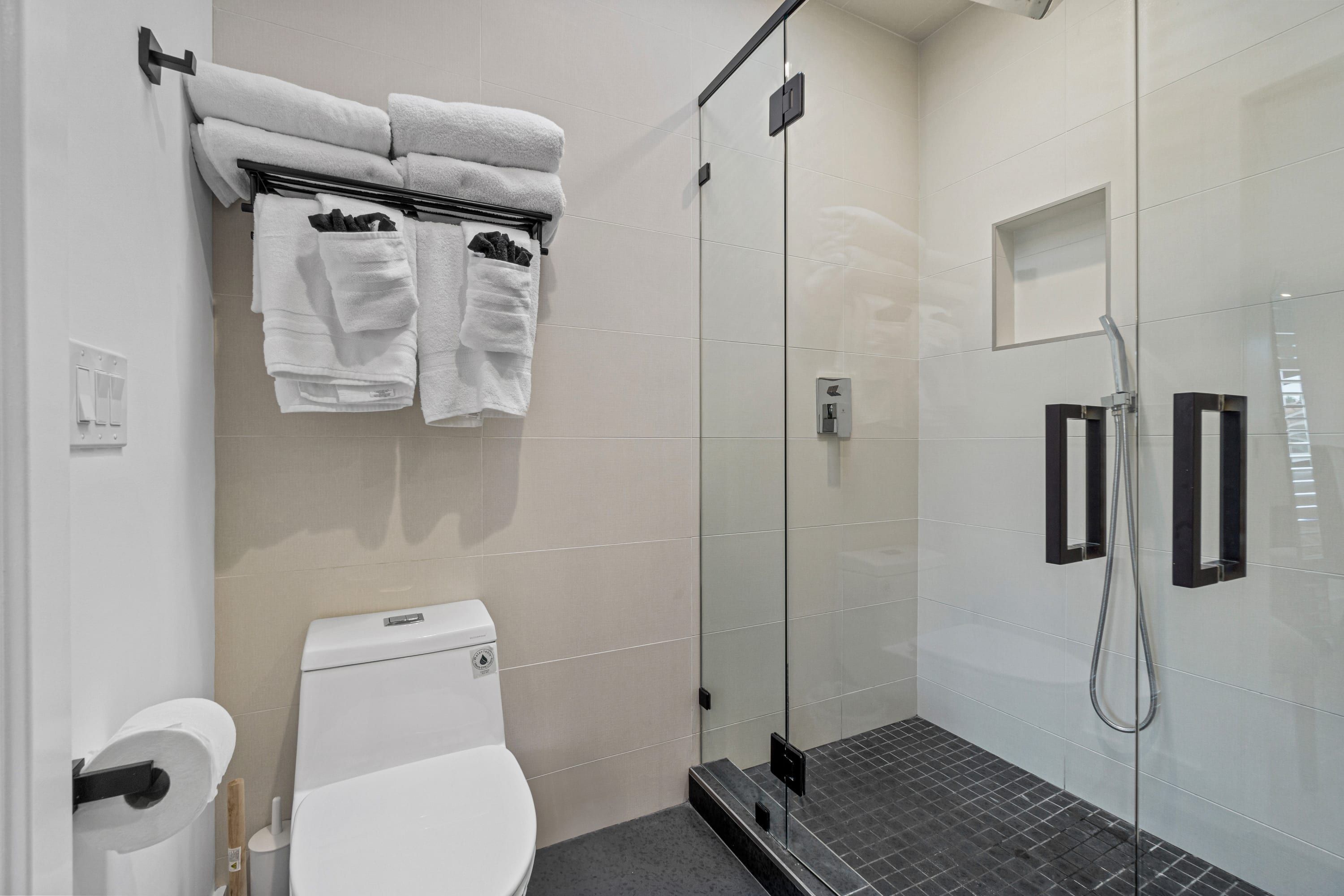 A modern bathroom with a glass shower enclosure, a toilet, and a towel rack with folded towels.